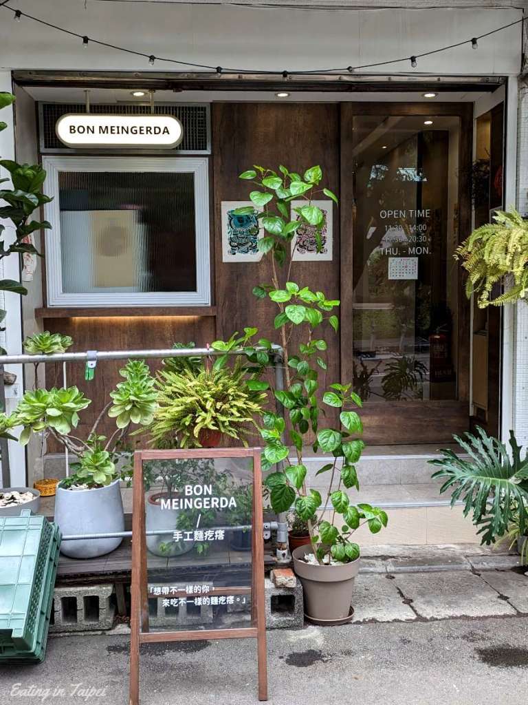 Bon Meingerda from the outside is littered with green plants and dark wood. It looks inviting, but warm and comfortable.